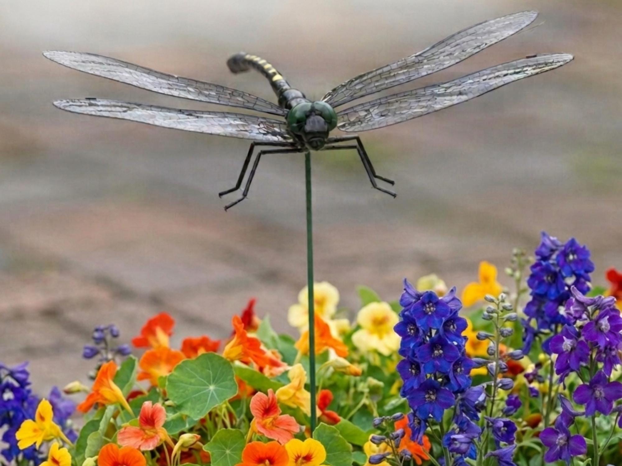 Realistic dragonfly plant stake displayed above bright flowers