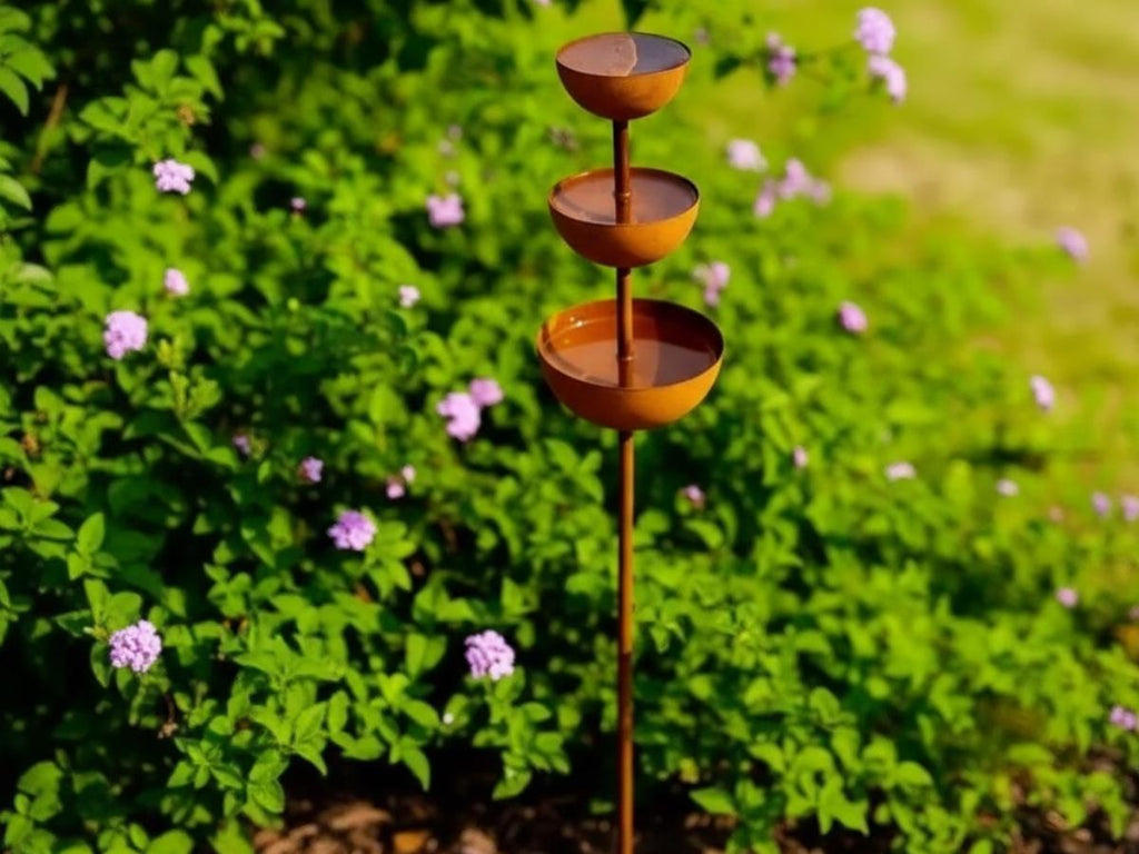 Rust metal three-bowl garden stake in a green flower bed