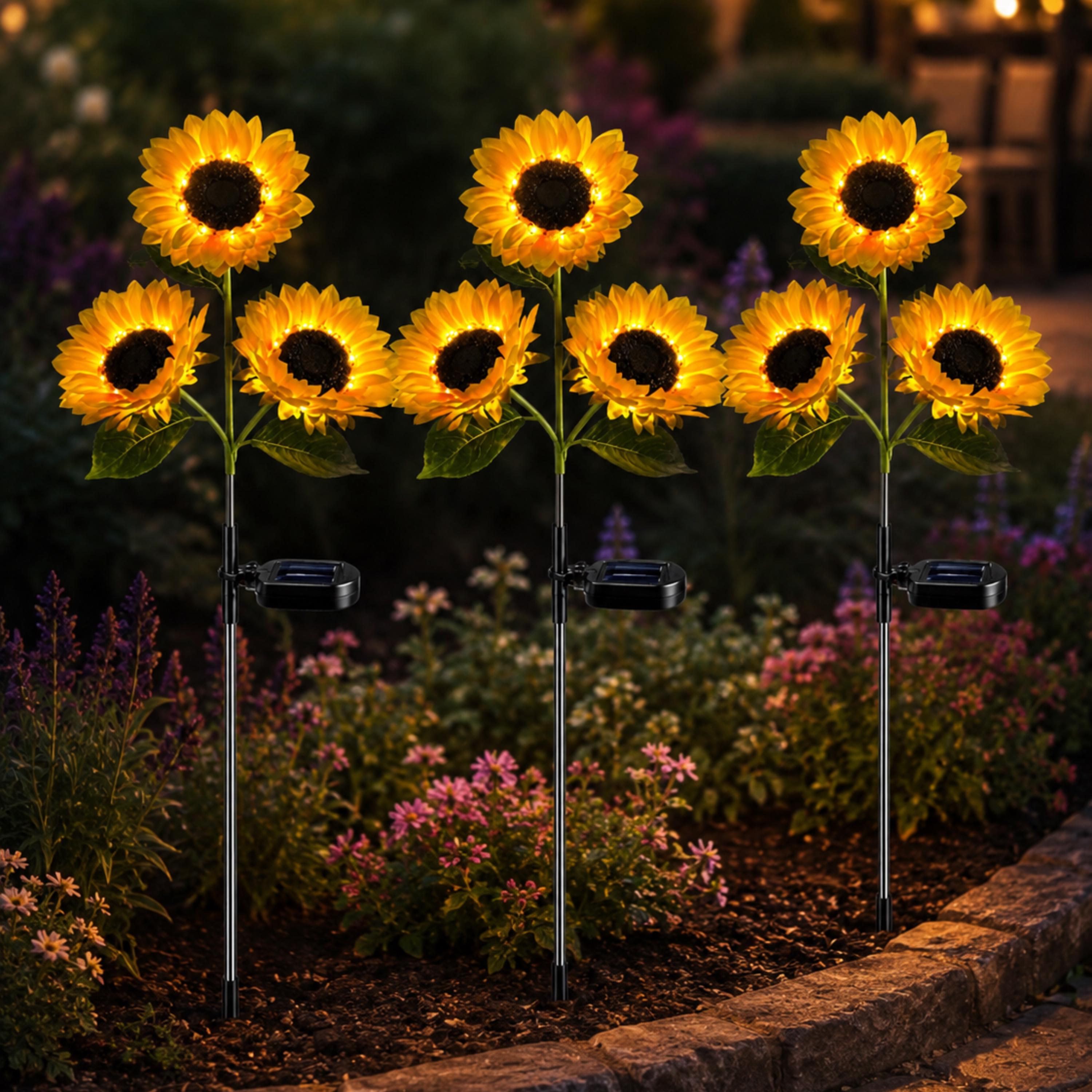 Three solar sunflower stakes glowing together in a garden at night