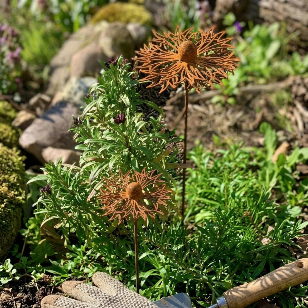 Two rusted metal flower stakes beside garden plants and stones