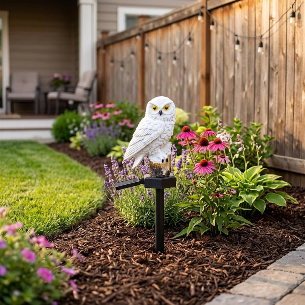 White solar owl light placed in a backyard flower border