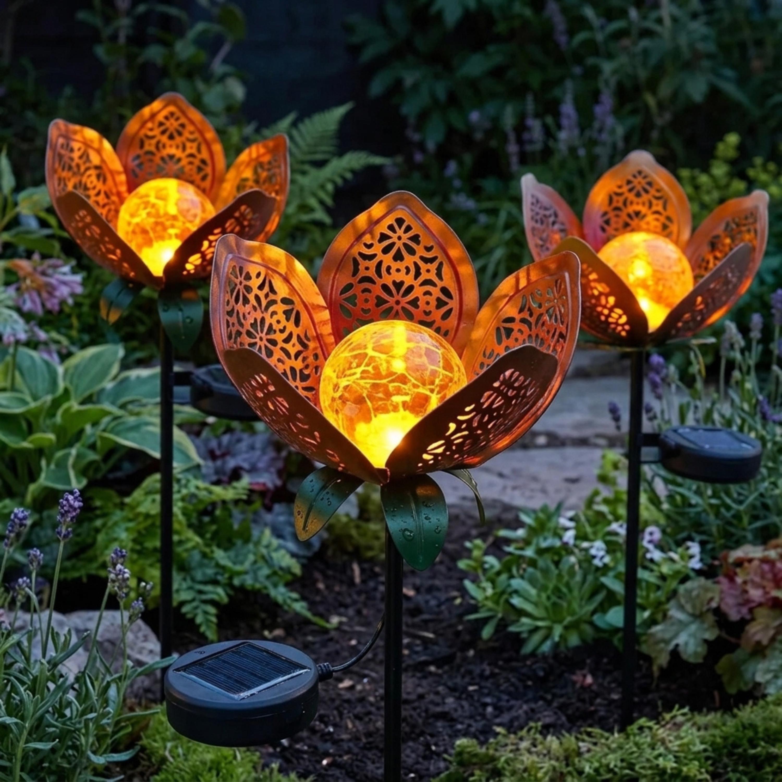 Three solar lotus stake lights arranged among garden plants