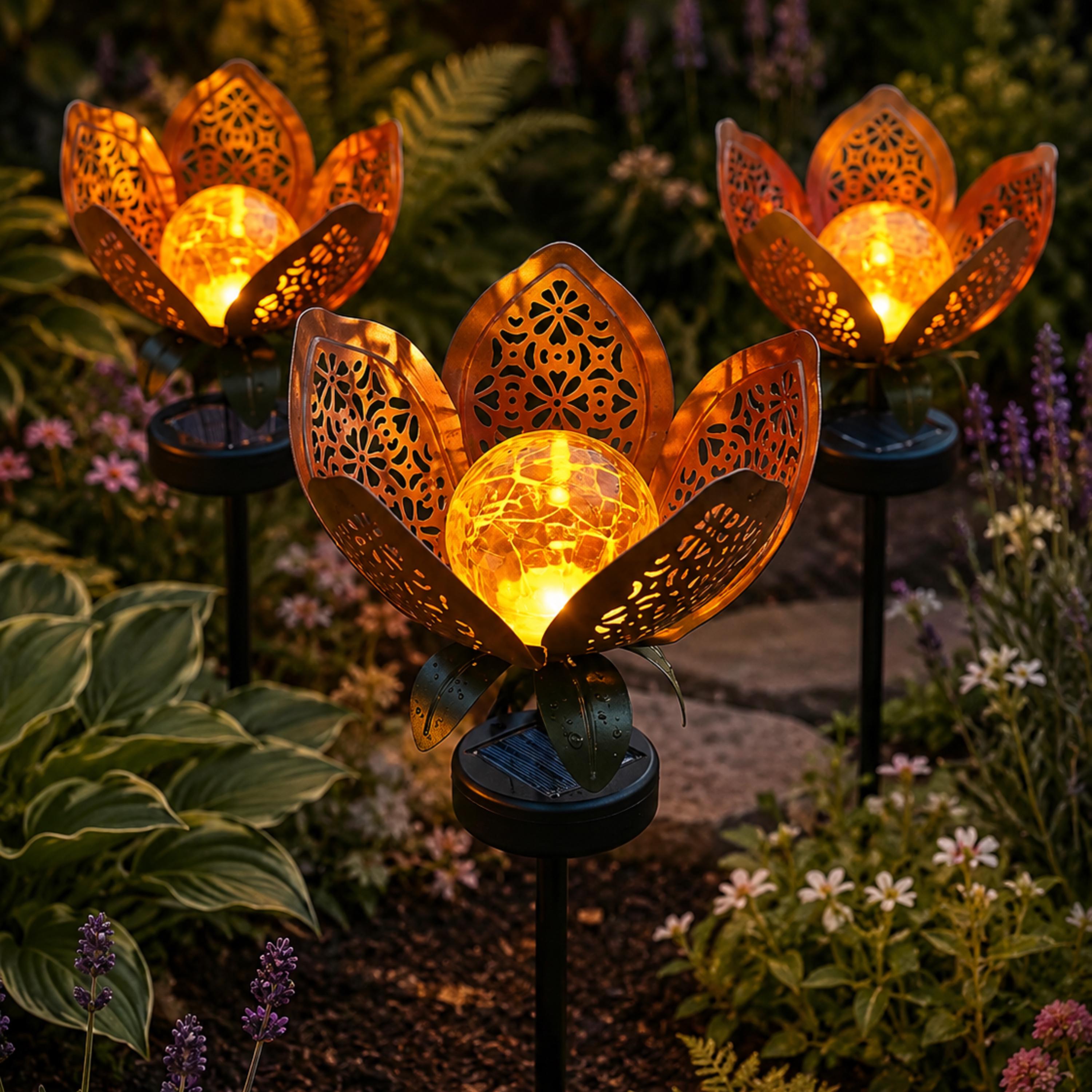 Three glowing solar lotus flower stake lights in a garden bed
