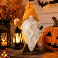Orange Halloween gnome holding a glowing black lantern beside pumpkins