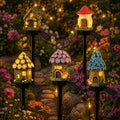 Five solar fairy house stake lights glowing in a colorful garden
